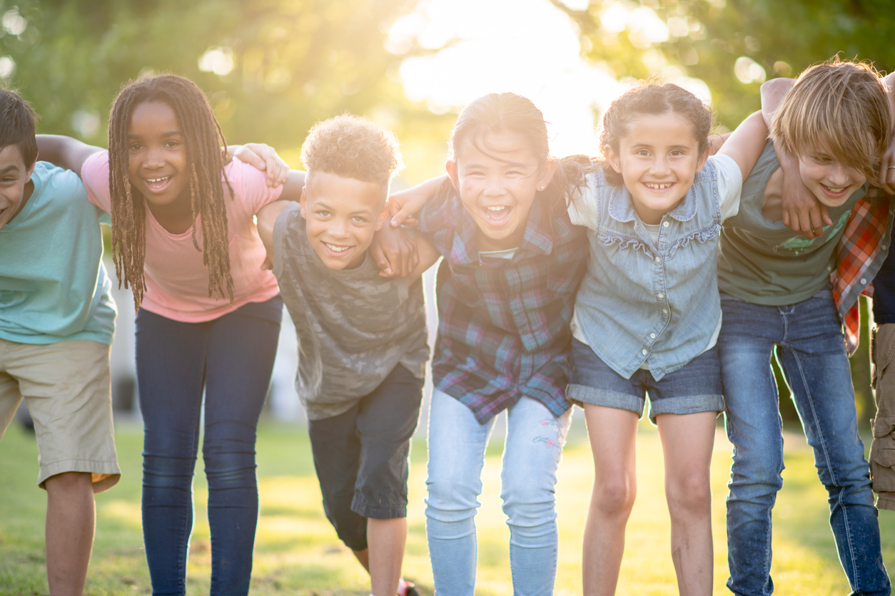 A beautiful multi ethnic group of elementary age children huddled together for a photo. They are embracing each other while smiling and laughing.