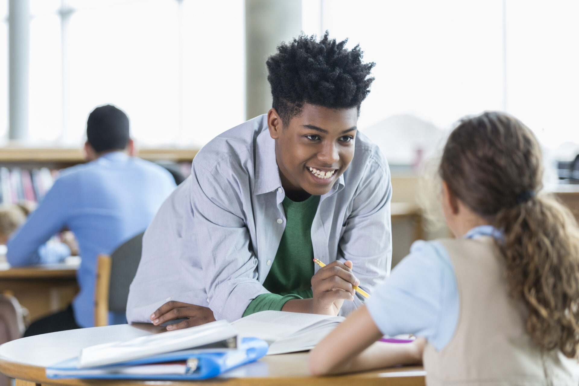 Confident African American male high school student works with an elementary student after school. He is helping the student with math homework.