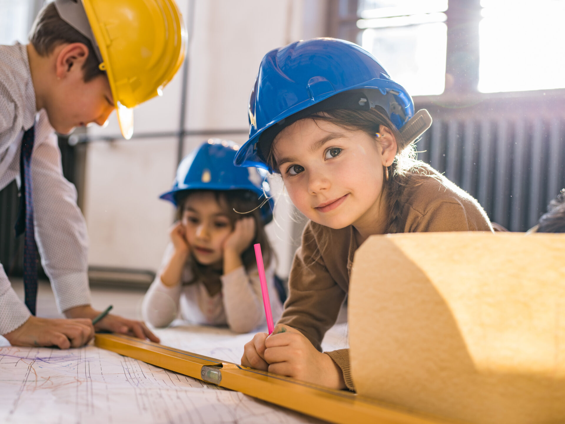 Group of little engineers working on blueprints in the office. Focus is on girl looking at camera.